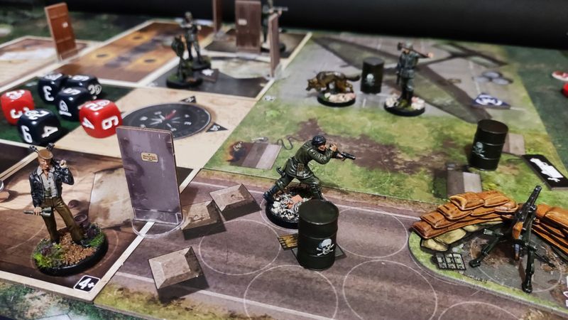 A board game map of a ww2 airfield. Painted commando, enemy, and dog miniatures are on the board, and dice and other components are in the background