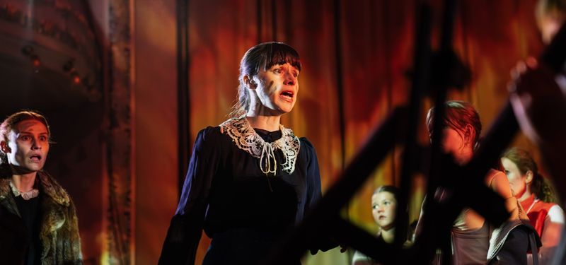 An actor, ash on her face, and clothes singed, giving an emotional response to the fire