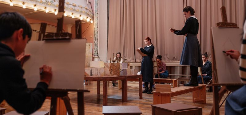 In the theatre space, actors and audience members work on drawing in an art class.