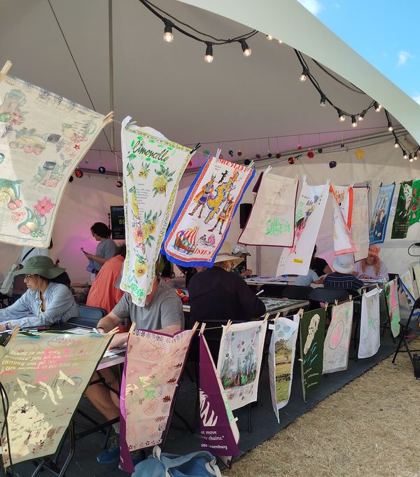 A collection of colourfully painted tea towels are hung alongside a marquee, drying gently in the breeze