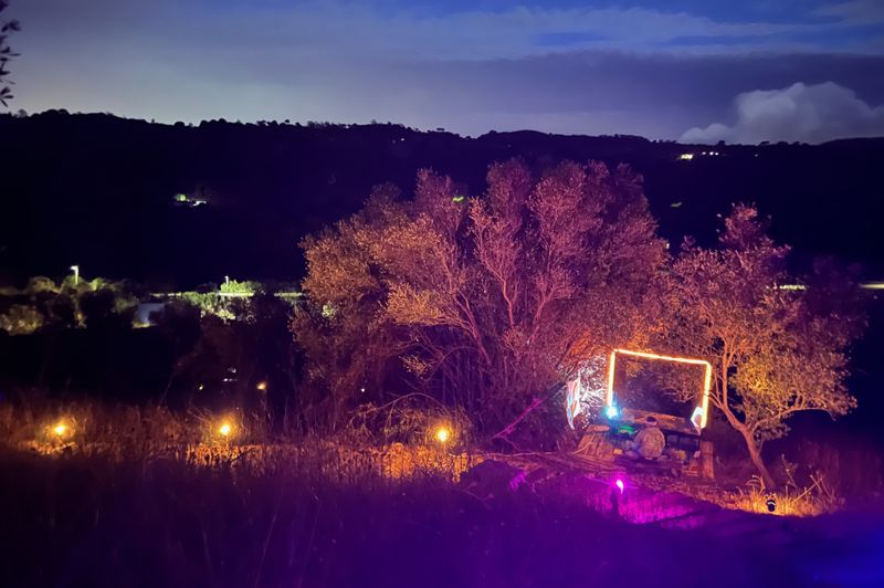 Photograph of an audience member lit by a giant mirrored display, the lit path in the foreground and valley at dusk at the rear.