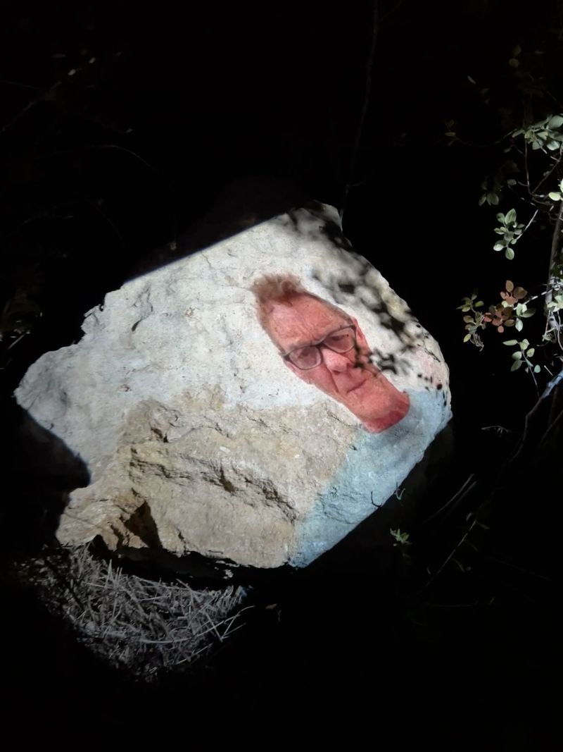 Photograph of an interview with an artist, projected onto the rocks and dirt where the artist worked years previously