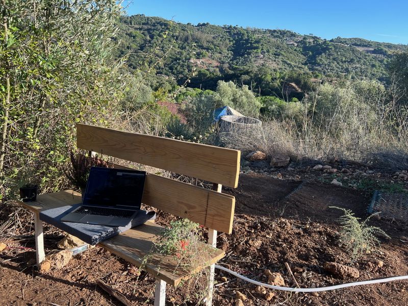 Photograph of a laptop on a bench near the top of the hill, overlooking the green valley below