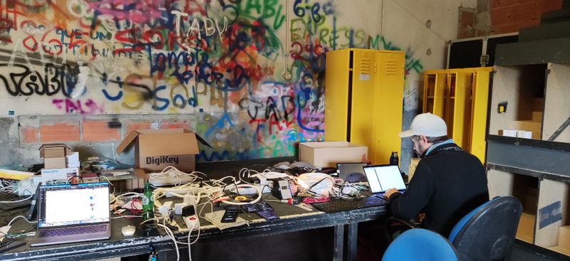 Photograph of Julian Jungel working coding, on a table surrounded by technology of different shapes and sizes.